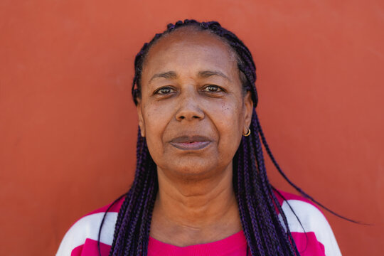 African senior woman with braided hair looking on camera with red background - Portrait of elderly person - Lifestyle and urban concept