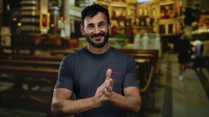 Hispanic man with a beard claps hands indoors in a beautifully lit catholic church setting,...