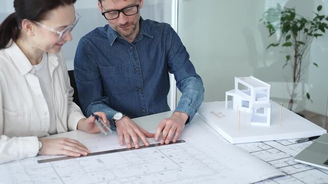 Architects engaging in a professional meeting, reviewing detailed blueprints on a table, utilizing a laptop, and collaborating on building design and construction planning