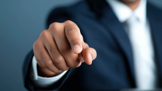 Businessman points at camera during meeting to emphasize important message while wearing suit in a modern office setting