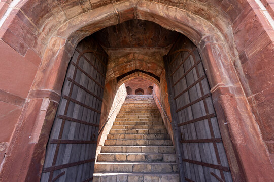 View of an ancient doorway with heavy gates opens onto a steep staircase leading upwards into the light, Delhi, Delhi Division, India.
