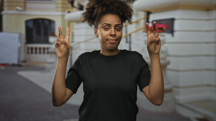 Young woman making air quotes with both hands and a wry smirk while standing in front of a building...