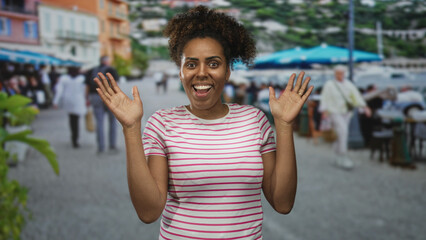 Fototapeta premium Woman raising both hands in an open palm gesture on a busy street terrace by an outdoor restaurant, smiling with face and hands visible; playful surprise.