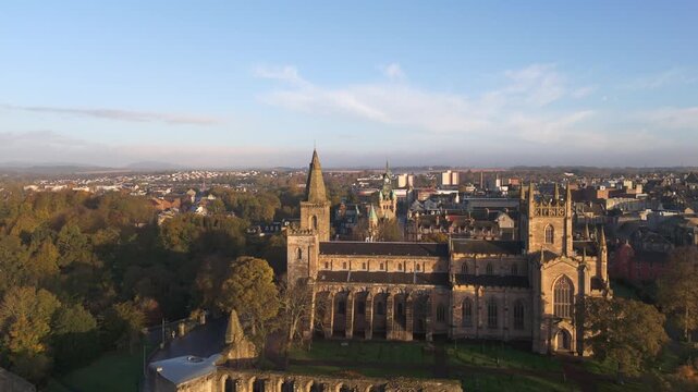 Aerial view of Dunfermline Abbey basks in the soft glow of dawn, its ancient stones standing proud amidst a tapestry of autumnal trees, Dunfermline, Scotland, United Kingdom.