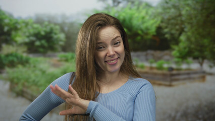 Obraz premium Woman hand wave gesture with tilted head and relaxed shoulders in forest clearing; joy playfulness laughter.