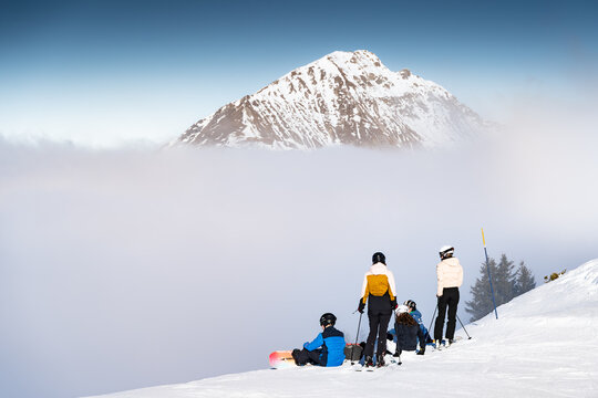 View of skiers pause on a snow-covered peak, gazing at a majestic, cloud-veiled mountain rising above the ethereal mist, Val-d Illiez, Valais, Switzerland.