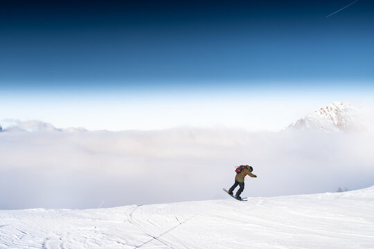 View of a snowboarder gliding down a snowy slope amidst a sea of clouds, with a majestic mountain peak piercing through the mist, Val-d Illiez, Valais, Switzerland.