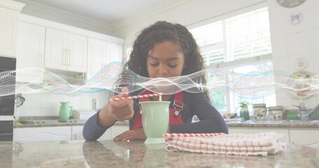 Stirring child wearing red overall straps at kitchen counter with green mug and striped spoon