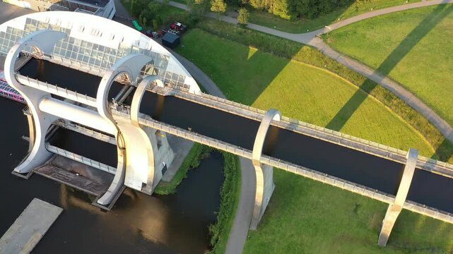 Aerial view of the Falkirk Wheel, a rotating boat lift connecting canals, standing as a testament to engineering amidst lush green landscapes, Falkirk, United Kingdom.