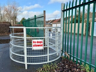 Metal pedestrian safety barrier with warning sign blocking access near a fenced walkway, urban infrastructure detail showing restricted entry and public safety control.