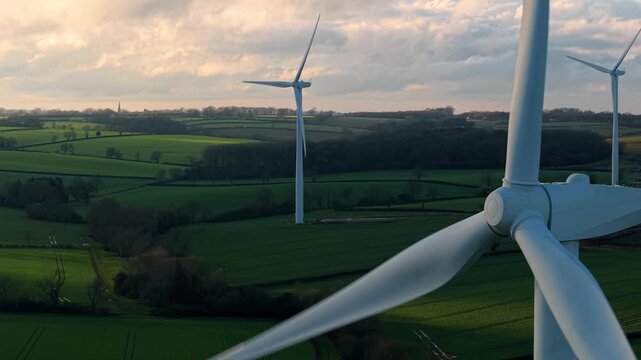 Aerial view of wind turbines standing tall against a backdrop of rolling green fields and a cloudy sky, Kelmarsh, Kelmarsh, United Kingdom.