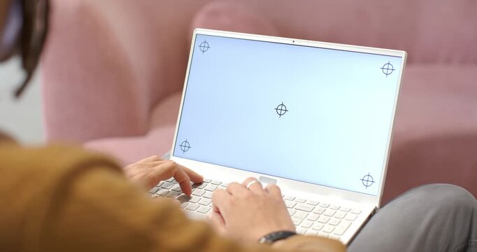 Hands are landing on white laptop keyboard and are softly typing for work on pink sofa