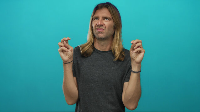 Man with long blond hair making finger quotes gesture with both hands and a skeptical expression in a studio; skepticism humor.