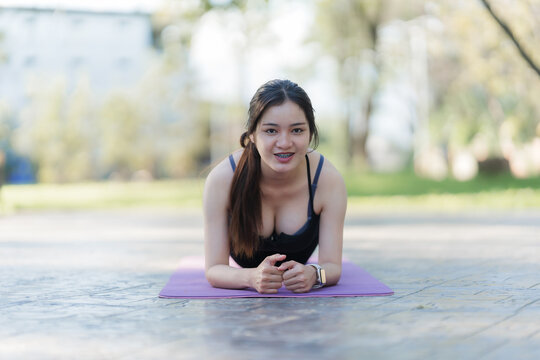 Wellness Warrior: A radiant woman strikes a plank pose on a purple exercise mat in an outdoor setting, exemplifying strength and health.