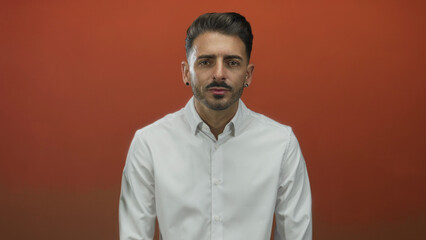 Obraz premium Man with uncovered face and white shirt looking directly at camera in bright orange studio; confidence.