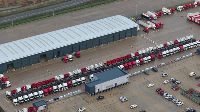 Aerial view of Royal Mail Midlands Super Hub revealing rows of neatly parked trucks and cars, contrasting with the grey building, Northampton, United Kingdom.