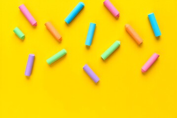Colorful chalks scattered on yellow surface for drawing and art education  various hues of pink purple blue green and orange sticks