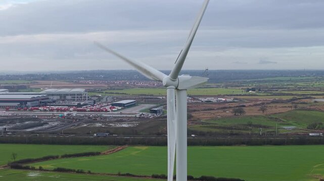 Aerial view of wind turbines standing tall over the green fields, contrasting with the industrial buildings in the distance, Yelvertoft, Crick, United Kingdom.