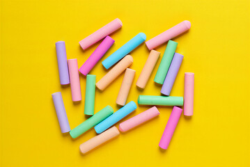 Pastel colored chalks scattered on yellow background  various hues of pink blue green purple and orange chalks strewn about