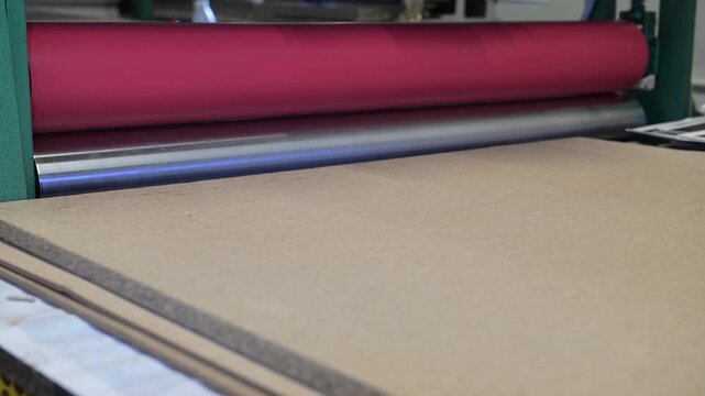 The rotating shafts of the industrial laminator in the printing house let posters through. Mechanics of rotation of metal shafts. Working hands at the machine