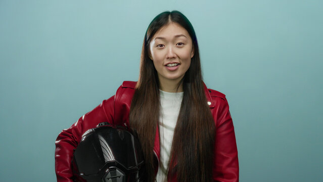 Woman in red jacket holding helmet against blue background looking thoughtful and confident in studio lighting with a refreshing appeal