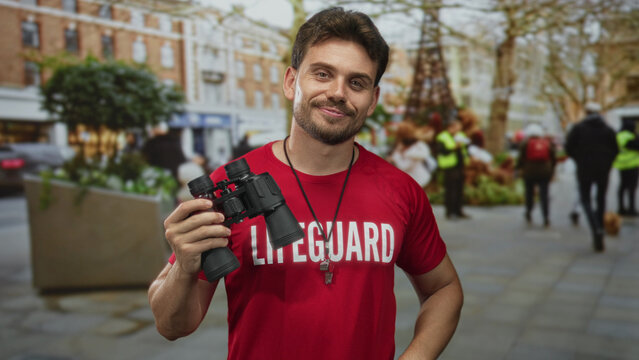 Man lifeguard smiling and holding binoculars with whistle necklace on busy city street; vigilance duty.