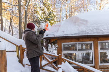 man clears the roof of thick layer of snow with snow shovel after a heavy snowfall in winter © Tatiana