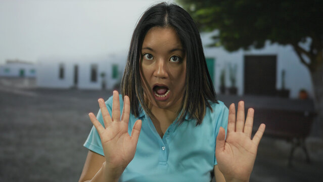 Woman expressing surprise outdoors in city street setting with hands raised, depicting shock or awe amid urban backdrop under daylight.