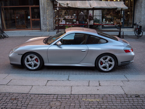 Porsche 911 Carrera 996 series silver coupe parked on city street with cobblestone, showing sports car luxury