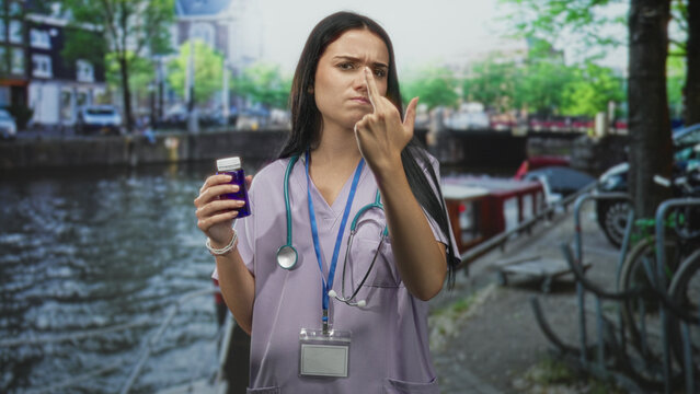 Woman nurse holding pill bottle and showing middle finger on canal street with stethoscope and badge, stern expression; defiance protest.