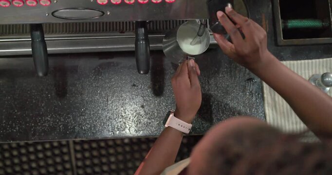 Steam wand is texturing milk in stainless pitcher while control knob is being turned at counter