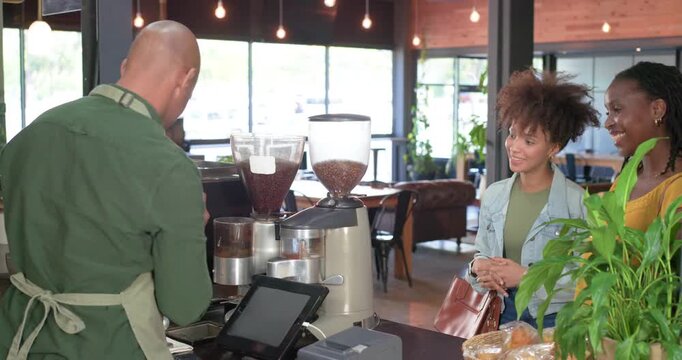 African American women ordering at cafe counter, barista grinding and handing cup, copy space