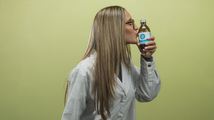 Woman in white lab coat kisses a bottled supplement while holding it up in studio; product appreciation playful.