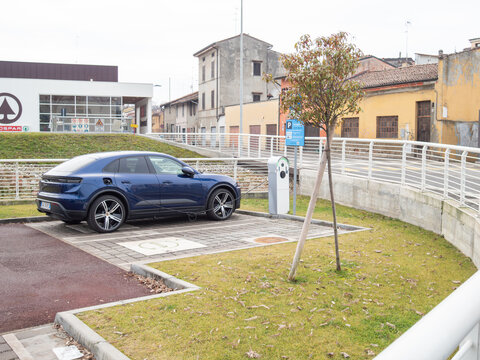 Blue Porsche Macan electric SUV charging at a public station, representing sustainable transportation and innovation