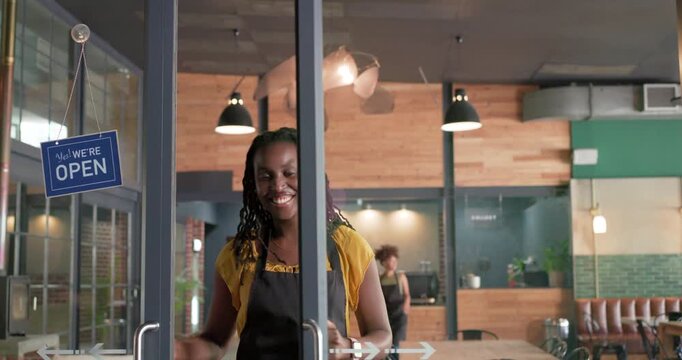 African American female baristas in aprons flipping closed sign pulling doors entering cafe opening