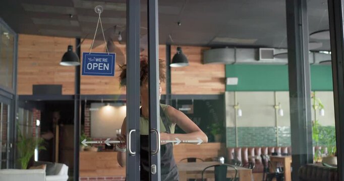 African American woman barista in apron flipping closed sign open, opening doors, preparing drinks
