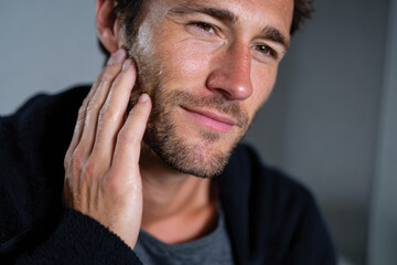 Fototapeta premium A man with a stylish beard gently touches his face, conveying a sense of tranquility and self-care in a softly lit environment that highlights his relaxed demeanor.