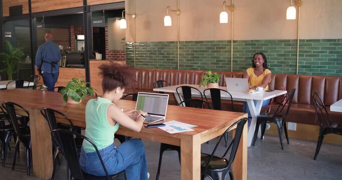 Women and barista greeting front woman resuming laptop typing, checking charts in cafe, copy space