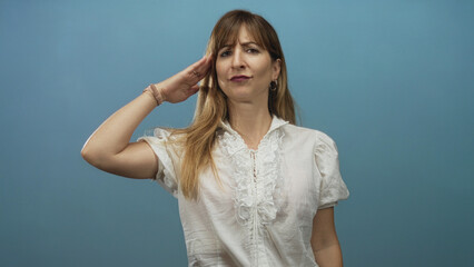 Young woman saluting with right hand to forehead in light blue studio wearing white ruffled blouse; sarcasm.
