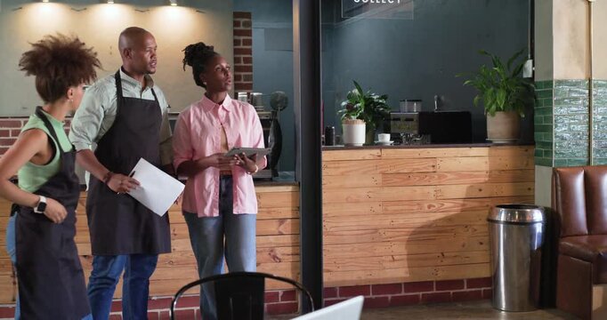 Diverse coworkers reacting to tablet alert, consulting paper at cafe, pointing, planning layout