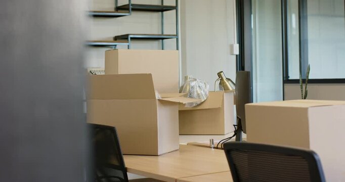 Obstruction sliding away is revealing open cardboard box on center desk, showing packing for move