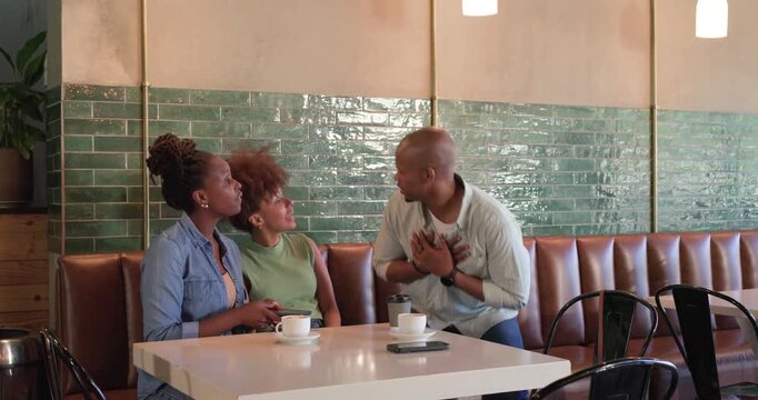 African American friends sitting cafe phone cups man touching chest greeting leaving with togo cup