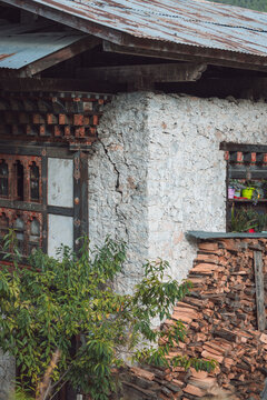 View of a weathered building corner shows textured white stucco, stacked firewood, and traditional Bhutanese architectural details, Jakar, Bumthang, Bhutan.