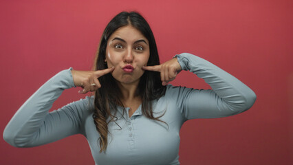 Obraz premium Young hispanic woman making funny faces over isolated red background wall showing playful and cheerful expression