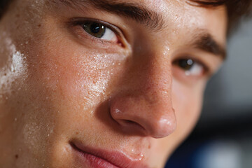 Naklejka premium This image captures a close-up view of a young man's face, glistening with sweat, reflecting determination and focus during a vigorous activity or workout session.