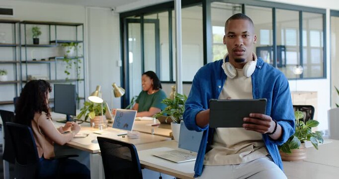 Colleagues at desk watching man in blue shirt scrolling tablet after reading message, laughing