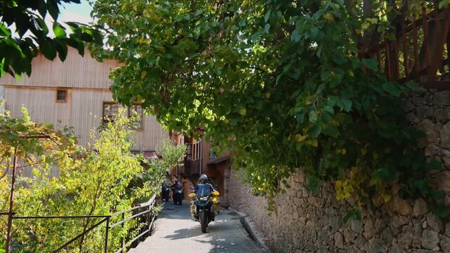 Motorcycle convoy riding through a village road in Erzincan, Turkey. Traditional houses, stone walls and autumn trees create a scenic rural atmosphere ideal for travel, adventure and cinematic road tr