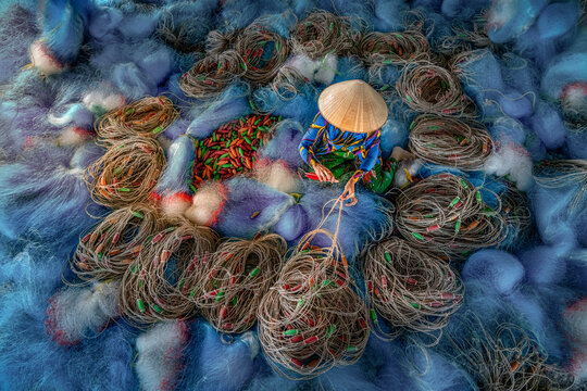 Fisher lady mending a sea of tangled blue fishing nets, Bac Lieu, Mekong Delta, Vietnam.