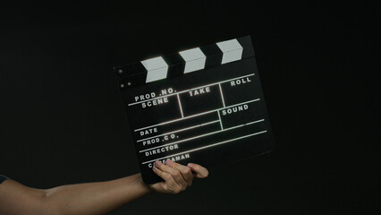 Naklejka premium Man holding film clapperboard against black background signifies filmmaking and production process.