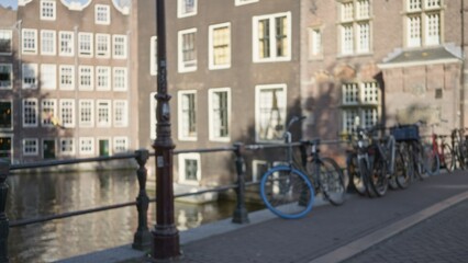 Blurred view of amsterdam canal with bicycles lined along the waterfront under soft sunlight highlighting iconic dutch architecture